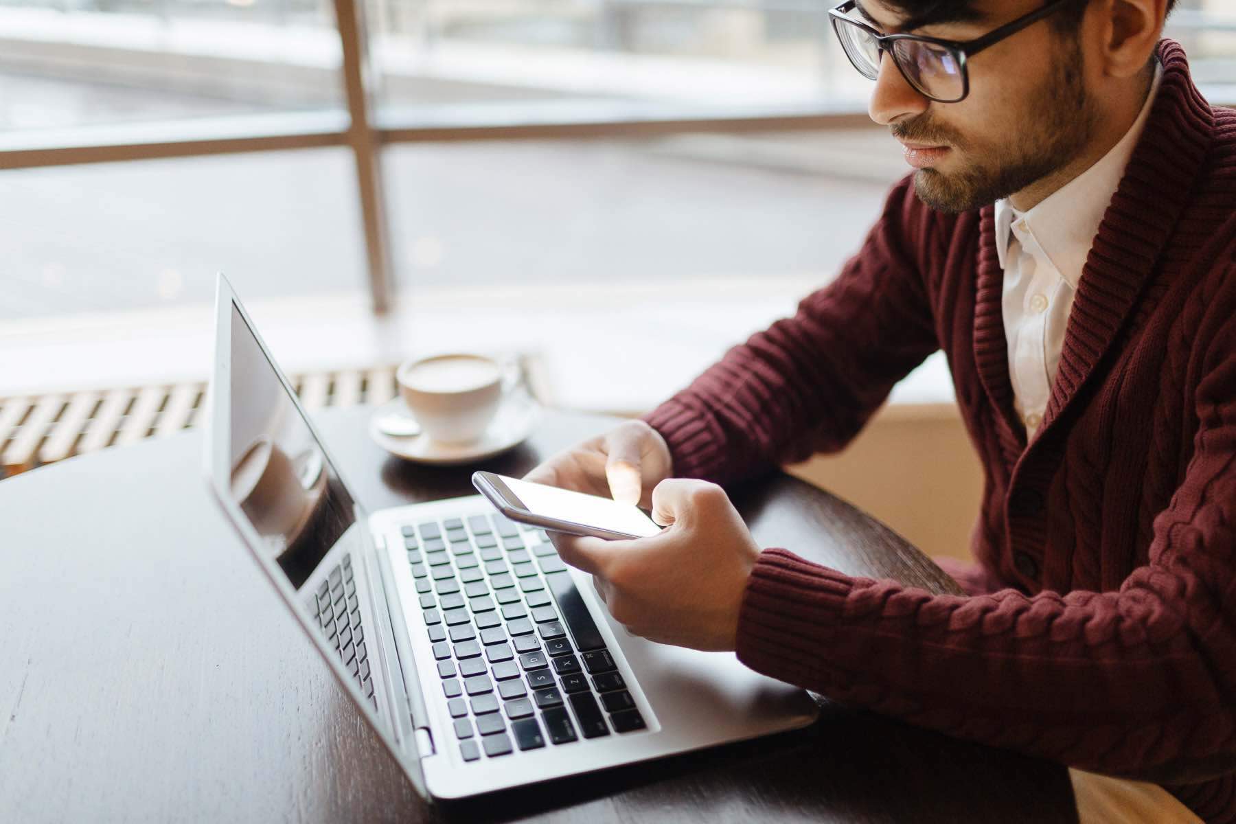 Young businessman messaging on smartphone in front of laptop
